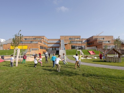 Der große Bildungsbau für ca. 800 Kinder und Jugendliche umfasst einen Kindergarten, eine Volksschule und Klassen für Schüler*innen mit besonderen Bedürfnissen. Am zentralen Hannah-Arendt-Platz im großen Stadterweitungsgebiet Seestadt Aspern gelegen, besticht der terrassenförmig angelegte Holzbau mit einem großzügigen Freiraumangebot, das viel Platz für Sport und Spiel bietet.